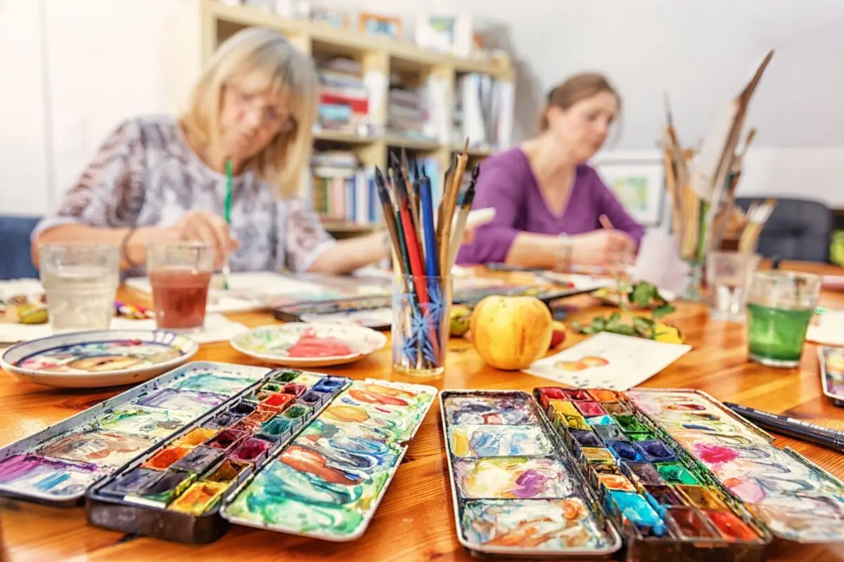 Zwei Frauen malen mit Aquarellfarben an einem Werktisch