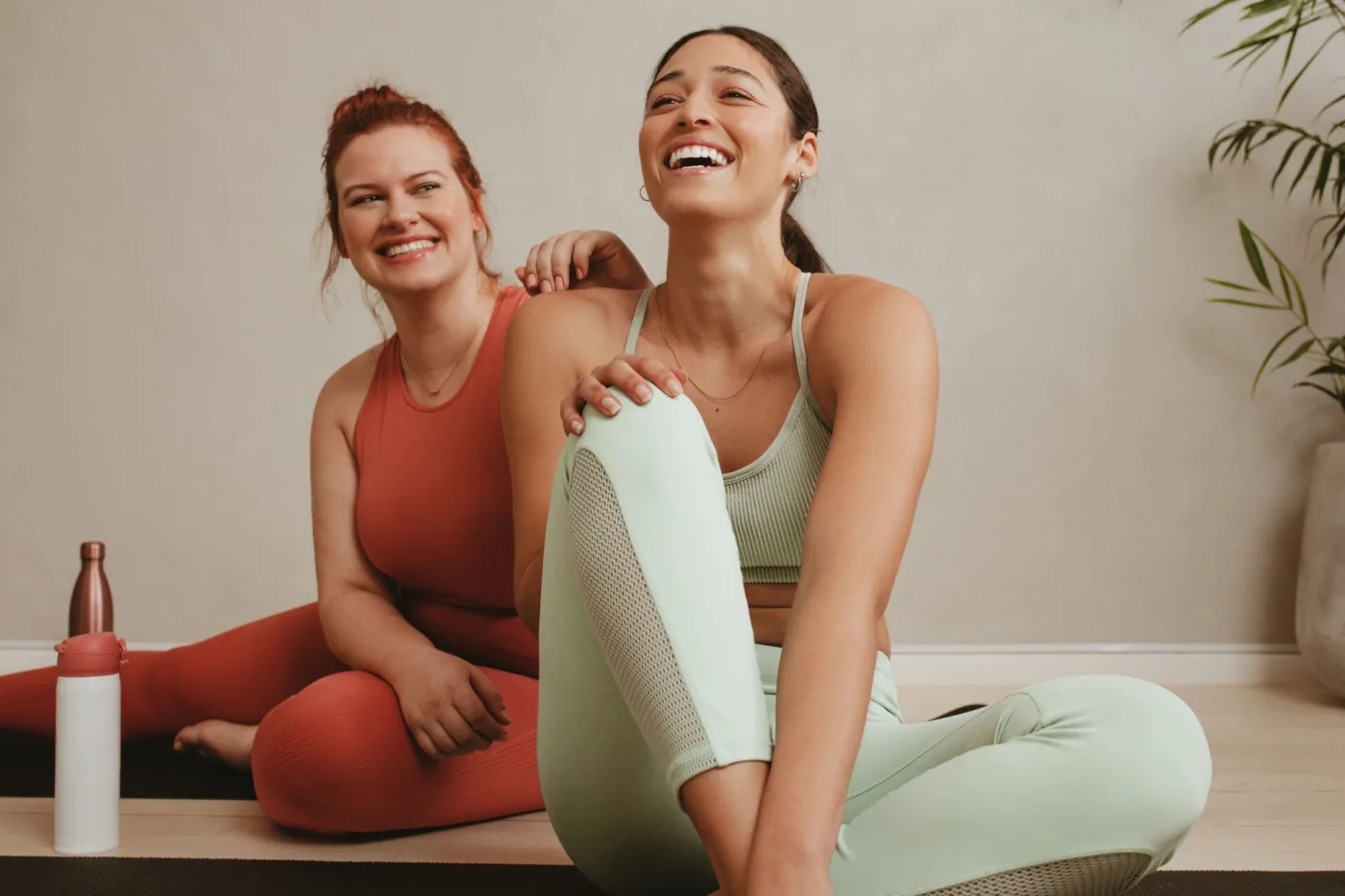 Zwei Frauen lachen auf ihren Yogamatten